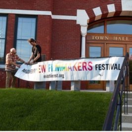 Two men attach an MNFF banner to the railing in front of Middlebury's Town Hall Theater