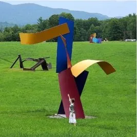 A woman reaching her hand up in front go a multi-colored statue, mimicking the statue's form