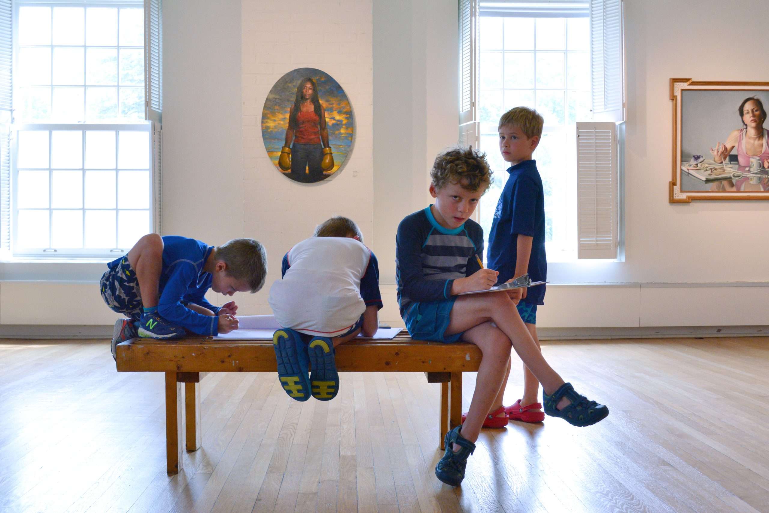 Four children in a bench in a bright gallery.
