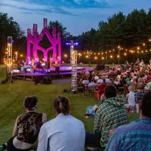 The crowd watches a performance on an illuminated outdoor stage.