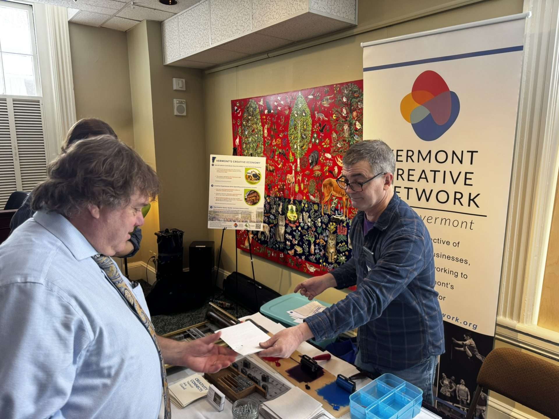 a person hands another person a print from the printmaking activity at Creative Sector Day