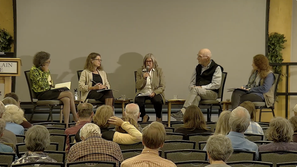 The event's five speakers sit together on stage for panel discussion while the audience watches. Alison Hawthorne Deming holds a microphone and speaks.
